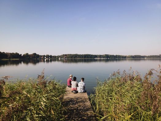 Drei Personen sitzen auf einem Steg am Großen Storkower See