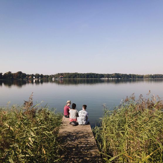 Drei Personen sitzen auf einem Steg am Großen Storkower See