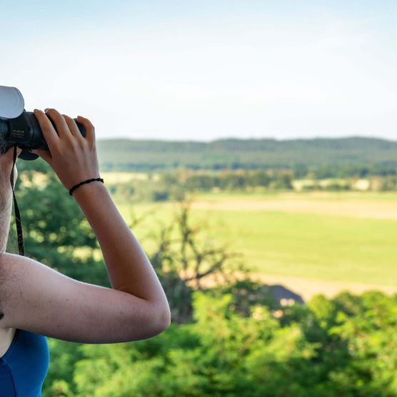 Eine junge Frau genießt mit einem Fernglas den Ausblick von der Carlsburg in Falkenberg