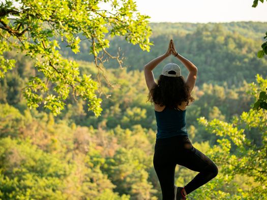 Frau steht auf einer Bank vor einem Wald und macht eine Yoga Figur