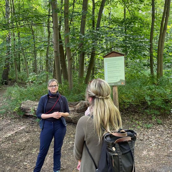 Zwei Personen stehen im Wald vor einer Tafel