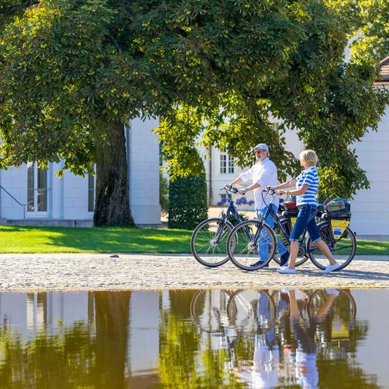 Zwei Radfahrer schieben ihre FahrrÃ¤der vor dem Schloss Neuhardenberg. Sie sind auf der Märkischen Schlössertour unterwegs.