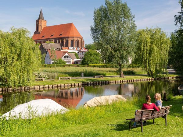 2 Personen auf der Bank am Spreeufer in Beeskow. Im Hintergrund die St. Marienkirche 