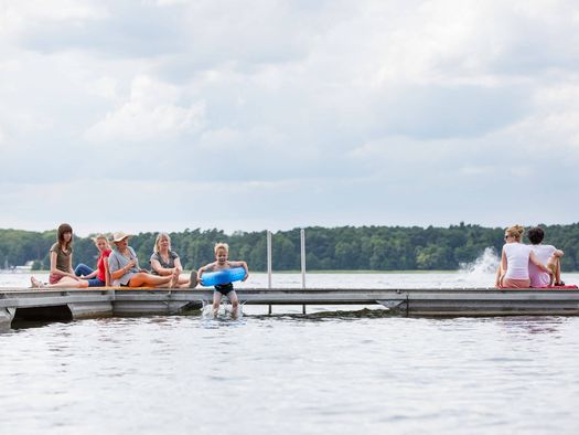 Ein Junge paddelt mit blauem Schwimmring und wird von einem älteren Mädchen schwimmend begleitet. 