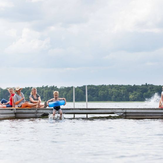 Ein Junge paddelt mit blauem Schwimmring und wird von einem älteren Mädchen schwimmend begleitet. 