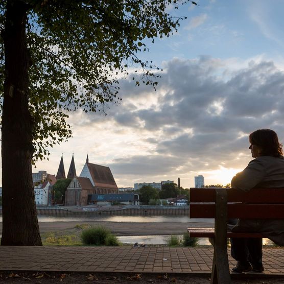 Frau sitzt auf eine Bank und blickt auf die abendliche Skyline von Frankfurt (Oder)