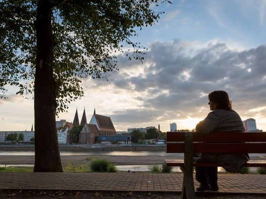 Frau sitzt auf eine Bank und blickt auf die abendliche Skyline von Frankfurt (Oder)