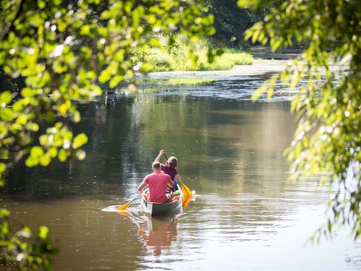 Eine junge Frau und ein junger Mann sitzen hintereinander in einem Kanu und paddeln Ã¼ber die Spree.