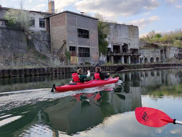 Menschen sitzen in einem Kajak und paddeln an einem Lost Place der Industiregeschichte vorbei