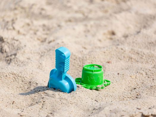 Ein grünes Buddel-Förmchen und eine blaue Schiffe liegen im Sand eines Strandes. 