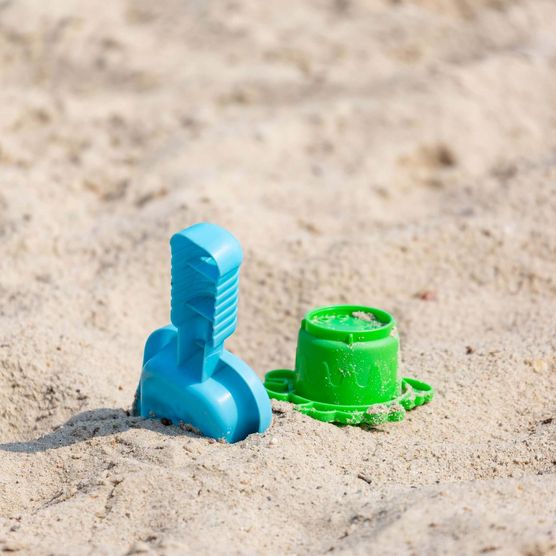 Ein grünes Buddel-Förmchen und eine blaue Schiffe liegen im Sand eines Strandes. 