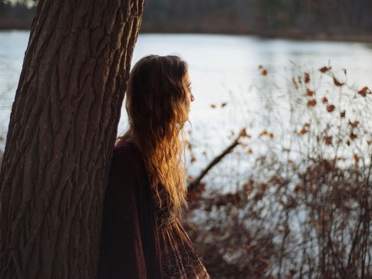 Slow Trip Angebot "Draußenseinzeit", Mensch schaut angelehnt an einem Baum auf einen See