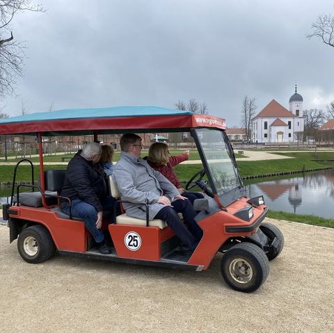 Vier Personen sitzen im Golfcar und schauen sich das Schlossgut an