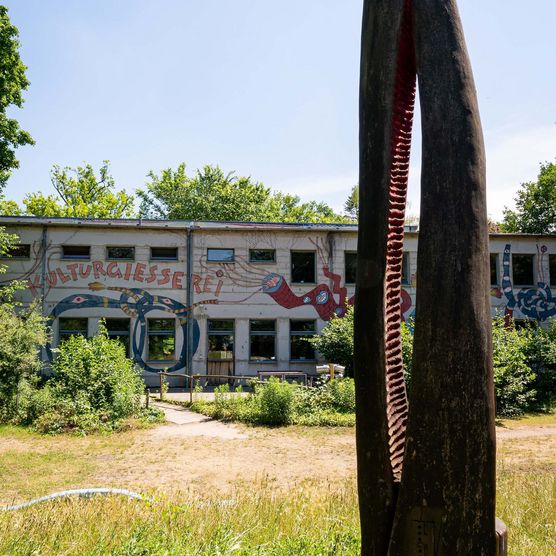 Blick an einer Skulptur vorbei auf ein Gebäude an dem "Kulturgiesserei" steht