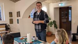 Der Künstler Ulrich Handke steht im Keller des Gutshauses vom Schloss Altlandsberg und erklärt den Teilnehmenden des Workshops "Kreativ-Druck", wie die Drucktechnik Monotypie funktioniert.